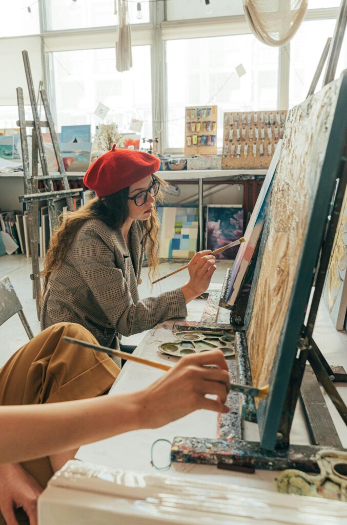 Young woman in beret painting on canvas in a light-filled art studio, capturing creativity.
